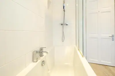 a white bathroom with a bath tub next to a door at The Old Bakery - Aldeburgh Coastal Cottages in Aldeburgh