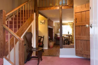 a hallway with a staircase and a chair in a house at Wren Cottage, a very cosy historic Coastal Cottage in a pretty little village in Wickham Market