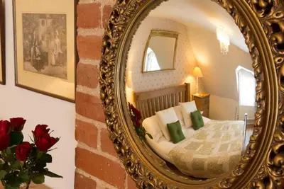 a mirror reflecting a bedroom with a bed with green pillows at Wren Cottage, a very cosy historic Coastal Cottage in a pretty little village in Wickham Market