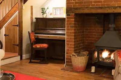 a living room with a brick fireplace with a piano at Wren Cottage, a very cosy historic Coastal Cottage in a pretty little village in Wickham Market