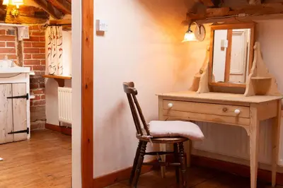 a chair sitting next to a wooden dresser with a mirror at The Bakery a honeymooners favourite cosy stylish with lovely walks and pubs in Edwardstone
