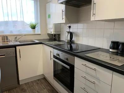 a kitchen with white cabinets and black counter tops at Modern Cosy Warm Home With Free Parking in Chelmsford