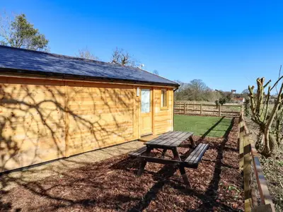 a wooden cabin with a bench next to a fence at Buttercup Lodge in Leiston