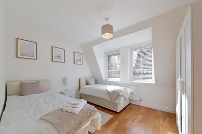 a white bedroom with two beds and a window at Spacious One Bed loft Apartment in Birchanger