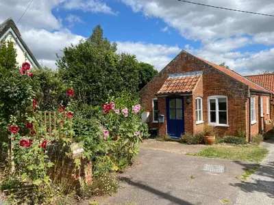 a brick house with a blue door and flowers at The Woodshed, Benhall in Saxmundham