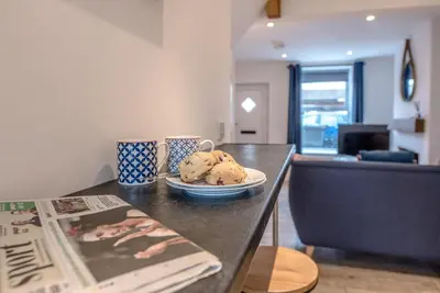 a table with a plate of cookies and a newspaper at Lily Cottage, Leiston in Leiston