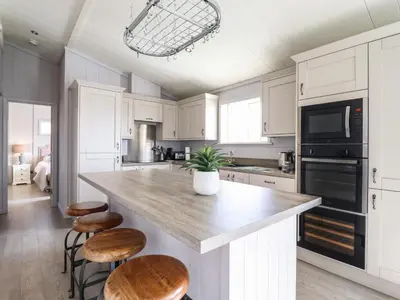 a kitchen with white cabinets and a large island with stools at Skylarks in Hengrave