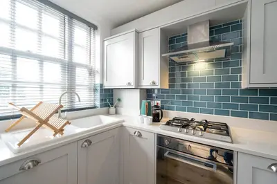 a kitchen with white cabinets and blue tiles at 15 Mill Field - Aldeburgh Coastal Cottages in Aldeburgh