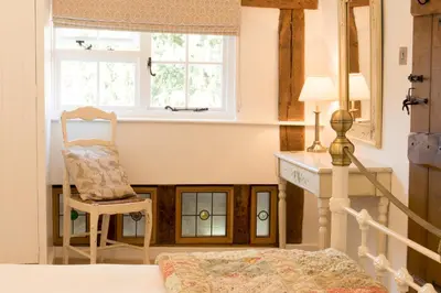 a bedroom with a bed and a chair and a window at Miller Cottage a luxury 1550's cottage in the Historic centre of Saffron Walden in Saffron Walden