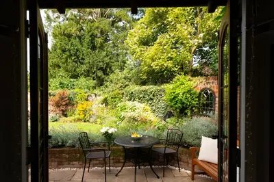 a patio with a table and chairs and a garden at Miller Cottage a luxury 1550's cottage in the Historic centre of Saffron Walden in Saffron Walden