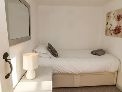 a small bedroom with a white bed and a lamp at 2 Greensleeves in Saxmundham