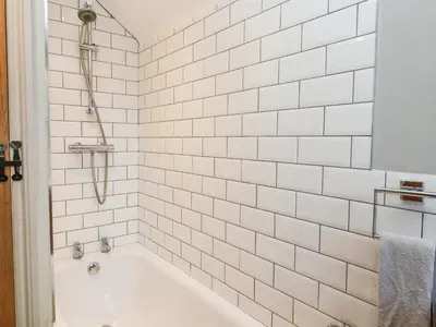 a bathroom with a bath tub with white tiles at 2 Greensleeves in Saxmundham