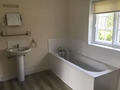 a bathroom with a bath tub and a sink at Thatched Cottage in Wix