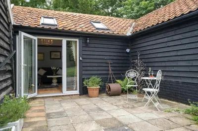 a black house with a patio with a table and chairs at The Cart Lodge - Aldeburgh Coastal Cottages in Wickham Market