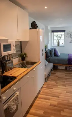 a kitchen with white cabinets and a living room with a couch at 121 Studio - Apartment with Kitchen, Terrace, Stansted Airport Shuttle in Bishops Stortford
