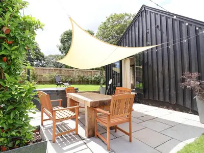 a backyard patio with a wooden table and chairs at Halcyon Barn, Wissett in Wissett