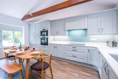 a kitchen with white cabinets and a wooden table and chairs at Ferry Corner Cottage, Sudbourne in Woodbridge