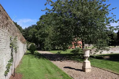 a stone vase sitting in the grass next to a wall at Garden House at Woodhall Estate in Hertford