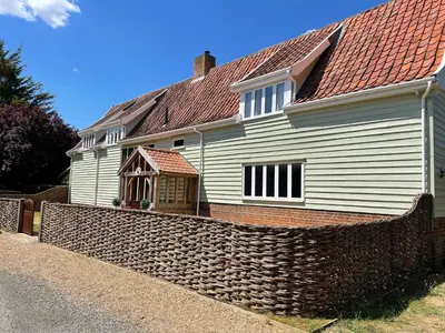 a white house with a stone fence in front of it at Moat Barn in Debach