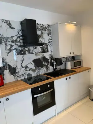 a kitchen with white cabinets and a marble wall at The old forge in Graveley