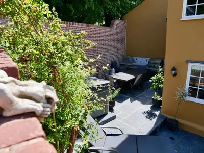 a patio with a table and chairs and a brick wall at Executive Suite with Private HotTub, Full SkyTV in 600 Year Old Manor House in Saffron Walden