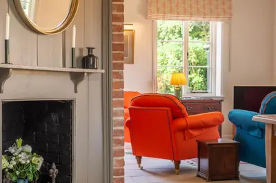 a living room with a red chair and a fireplace at Luxurious rural retreat - Holt Coach House in Sudbury