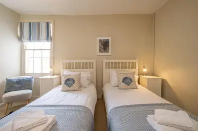 a bedroom with two beds and a chair and a window at Shore View, Aldeburgh - A lovely Seafront House on famous Crag Path with uninterrupted Beach Views - Aldeburgh Coastal Cottages in Aldeburgh