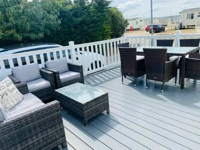 a deck with wicker chairs and a table and a table and chairs at Shell Beach Holiday Home Mersea Coopers Beach in East Mersea