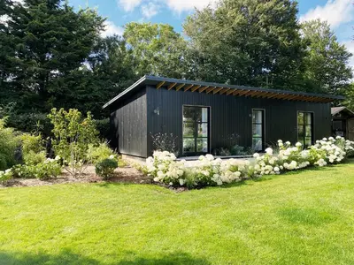 a black tiny house with white flowers in a yard at Little Owl by The Suffolk Cottage Collection in Aldeburgh