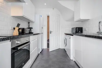 a white kitchen with white cabinets and a sink at Bright and spacious home with free parking and garden in Mountnessing
