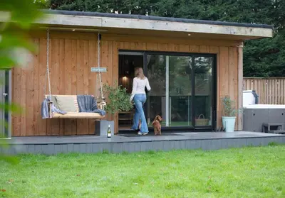 a woman standing on a porch with a dog at City to Country Retreat Luxury Lodges with Hot Tub, BBQ, Fire Pit in Toppesfield