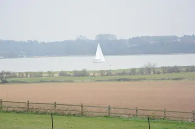 a sailboat on the water with a field and a field at Upper Lodge, Shotley in Chelmondiston
