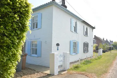 a white house with blue windows and a hedge at Vesta Cottage, Orford in Orford