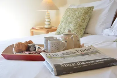 a tray of food and a newspaper on a bed at Pebble Beach Cottage, Aldeburgh in Aldeburgh