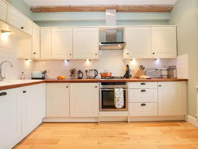 a kitchen with white cabinets and wooden floors at Saffron, Blythview in Blythburgh