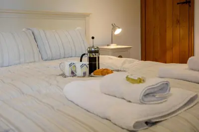a white bed with towels and a bottle on it at Two Chantry Barns, Orford in Orford