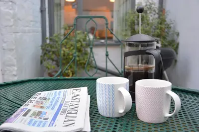 a table with two coffee cups and a newspaper at Gosfield Cottage, Aldeburgh in Aldeburgh