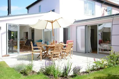 a patio with a table and chairs and an umbrella at 2 Pink Cottages, Aldeburgh in Aldeburgh