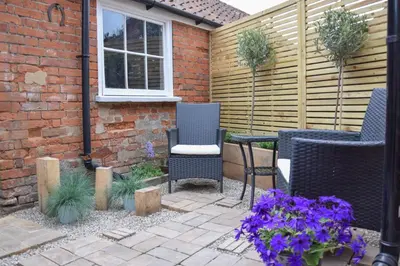 a patio with two chairs and a table and flowers at Arlo Cottage, Orford in Orford