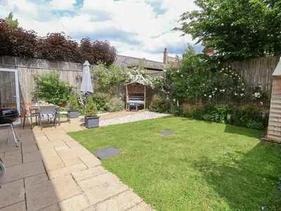 a backyard with a lawn with a table and an umbrella at 1 Coconut Cottage, Long Melford in Long Melford