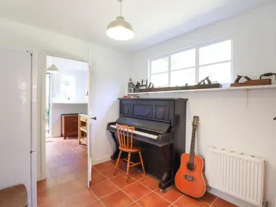 a living room with a piano and a guitar at Warren Cottage in Leavenheath