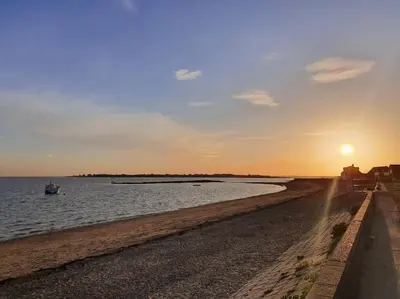 a boat in the water near a beach with the sunset at The Tiny Sea Gem in Jaywick Sands