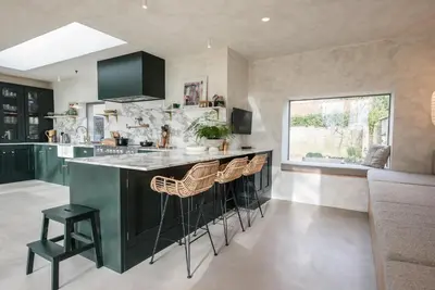 a kitchen with green cabinets and a counter with stools at The Limes, Benhall in Saxmundham