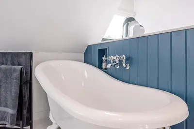 a white bath tub in a bathroom with blue tiles at Little Honey Pot, Benhall in Saxmundham