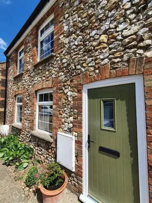 a brick house with a green door and a stone building at Belle Vue Cottage in Downham Market