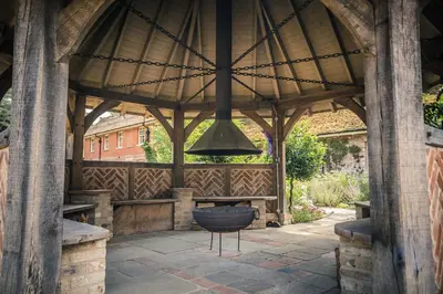 a large wooden gazebo with a grill in it at Lynford Holiday Cottages nestled in the heart of Thetford Forest in Mundford