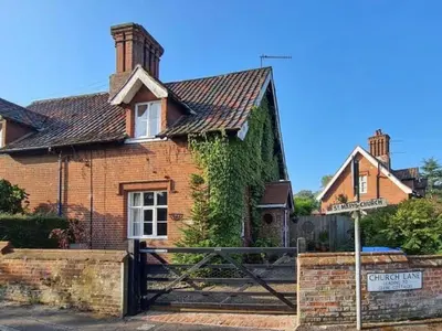 an old brick house with a sign in front of it at Corner Cottage in Alburgh