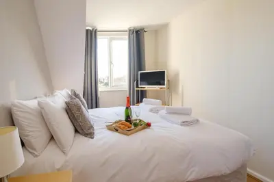 a white bed with a bottle of wine and fruit on it at 61 Fairfield Road in Aldeburgh