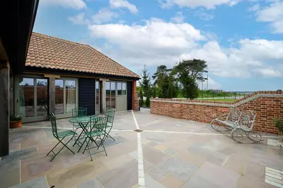 a patio with chairs and a table and a brick wall at Alde Bay Farm - Coral Cottage in Aldeburgh