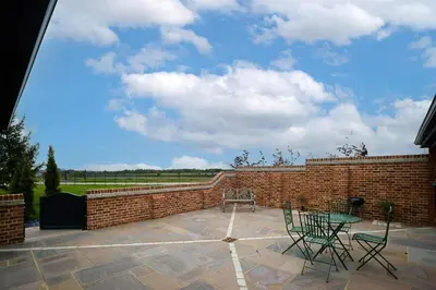 a patio with a table and chairs and a brick wall at Alde Bay Farm - Coral Cottage in Aldeburgh
